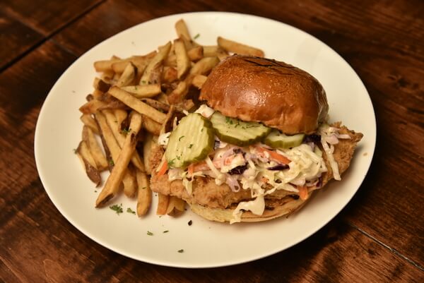 Chicken sandwich with coleslaw and pickles on a white plate with fries