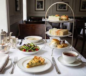 Elegant afternoon tea spread with sandwiches, pastries, salad, and tea.
