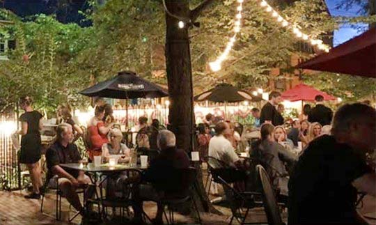 Reynolds Tavern outdoor dining area with people seated at tables under umbrellas at night.