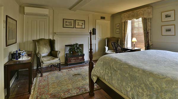 Antique-style bedroom with a four-poster bed, fireplace, and armchair.
