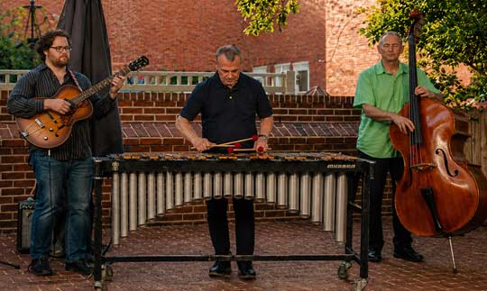 Three men playing a marimba, guitar, and cello in an outdoor setting
