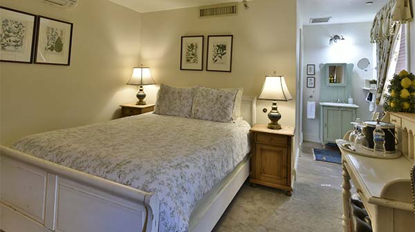 Cozy bedroom with a floral comforter, antique furniture, and a glimpse of a bathroom.