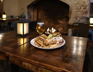 Pulled pork sandwich with fries and beer by fireplace