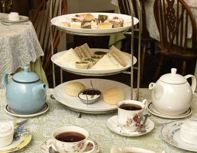 Three-tiered stand with tea, scones, and sandwiches on a dining table