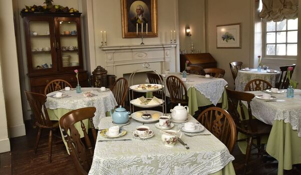 Dining room with tables set for tea, teapots, cups, and saucers, wooden chairs, and a fireplace