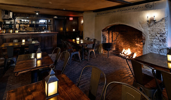 Cozy interior of The 1747 Pub with a fireplace, wooden tables, and lanterns