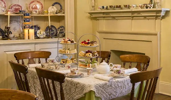 Elegant afternoon tea setup with tiered cakes, scones, and teacups on a lace-covered table.