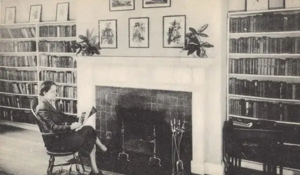 Woman reading in a library with bookshelves and a fireplace at Reynolds Tavern
